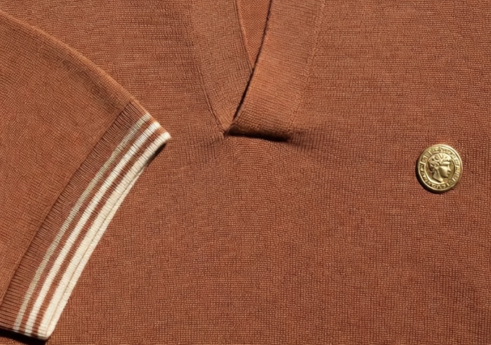 Terracotta knit polo with cream-striped trim and a gold coin button
