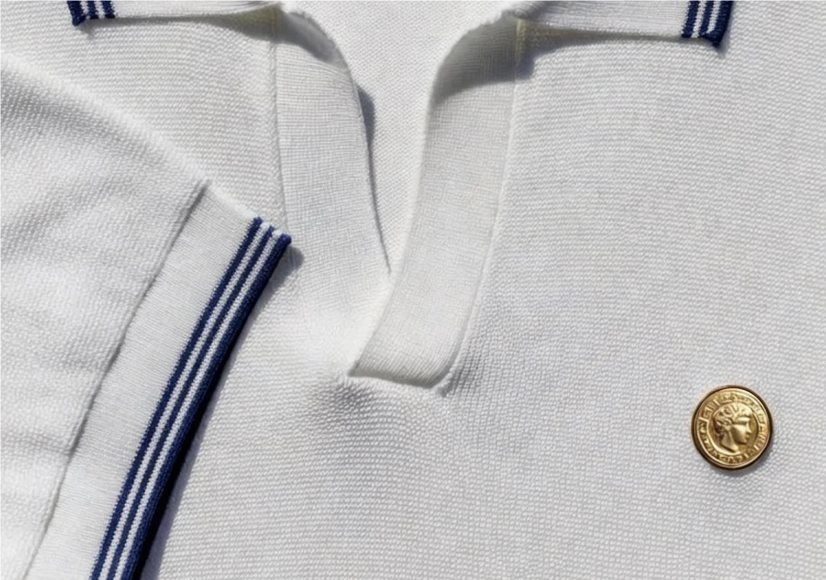 White knit polo with navy-striped trim and a gold coin button