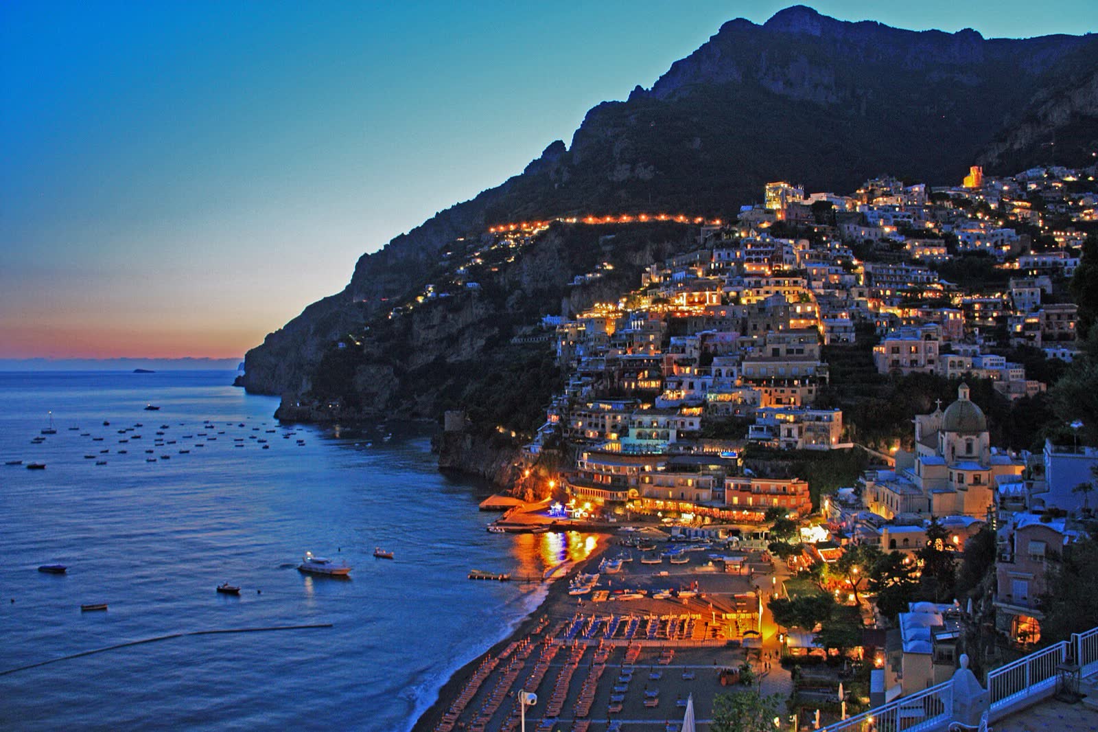 Positano lit up at dusk above the sea